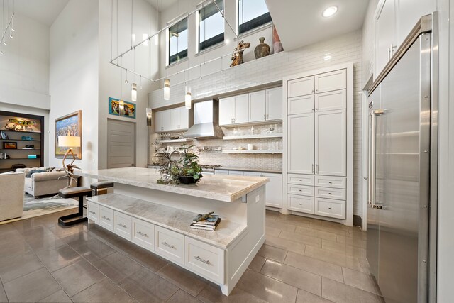 507 Terrace Dr, Houston, TX 77007 - kitchen with a high ceiling, high end refrigerator, wall chimney exhaust hood, white cabinetry, and tasteful backsplash