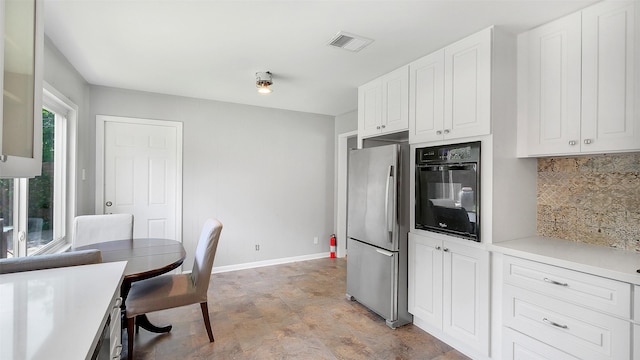 6805 Mobud Dr, Houston, TX 77074 - kitchen with freestanding refrigerator, black oven, tasteful backsplash, baseboards, and white cabinetry
