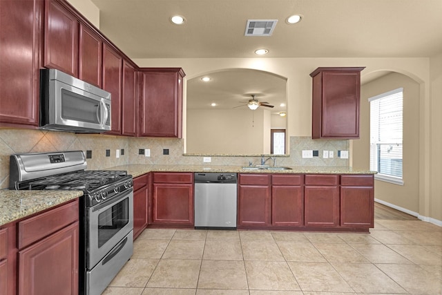 24734 Colonial Maple Dr, Katy, TX 77493 - kitchen with stainless steel appliances, dark brown cabinets, a ceiling fan, arched walkways, and decorative backsplash