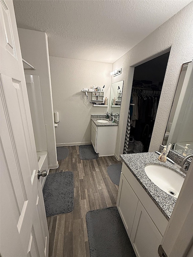 2009 6th St, Hempstead, TX 77445 - full bathroom featuring wood finished floors, a textured wall, a textured ceiling, two vanities, and a walk in closet