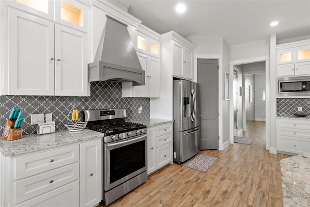 18327 Cypress Hill Dr, Rosharon, TX 77583 - kitchen featuring stainless steel appliances, custom range hood, white cabinetry, backsplash, and light wood-style flooring