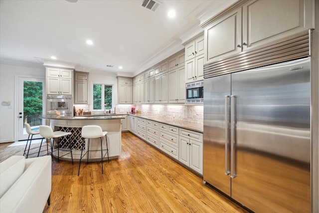5710 Logan Ln, Houston, TX 77007 - kitchen featuring built in appliances, ornamental molding, light wood-style flooring, backsplash, and a breakfast bar