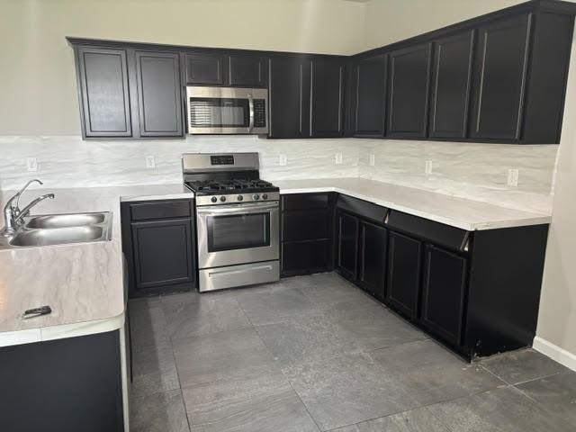 5426 Redwood Summit Ln, Katy, TX 77449 - kitchen featuring stainless steel appliances, a sink, dark cabinets, tasteful backsplash, and light countertops