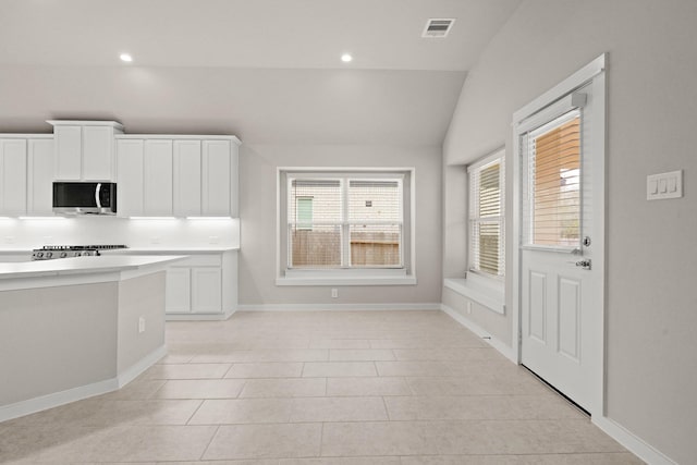 207 Little Dog Dr, Montgomery, TX 77356 - kitchen featuring stainless steel microwave, vaulted ceiling, light countertops, white cabinetry, and tasteful backsplash