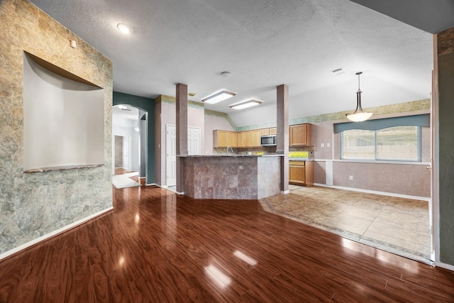 2723 Shelby Dr, Pearland, TX 77584 - kitchen featuring arched walkways, lofted ceiling, stainless steel microwave, light wood-style floors, and a textured ceiling