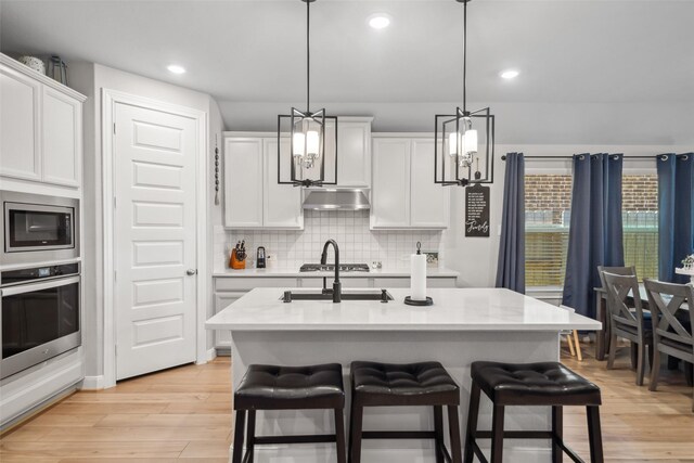 512 Highland Thicket Dr, Montgomery, TX 77316 - kitchen featuring stainless steel appliances, a chandelier, under cabinet range hood, a breakfast bar, and light wood-type flooring