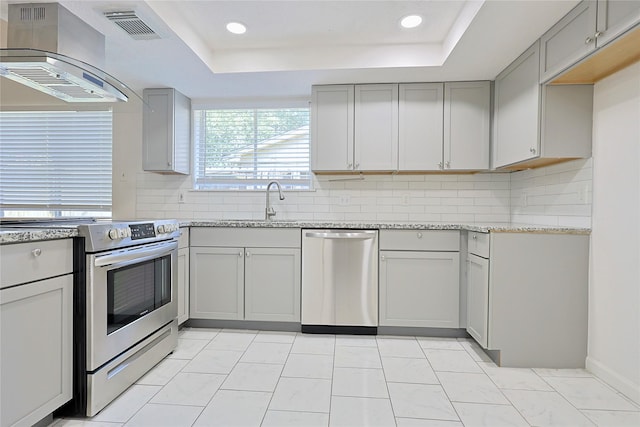 9910 Kent Towne Ln, Sugar Land, TX 77498 - kitchen with stainless steel appliances, wall chimney exhaust hood, gray cabinets, a tray ceiling, and recessed lighting