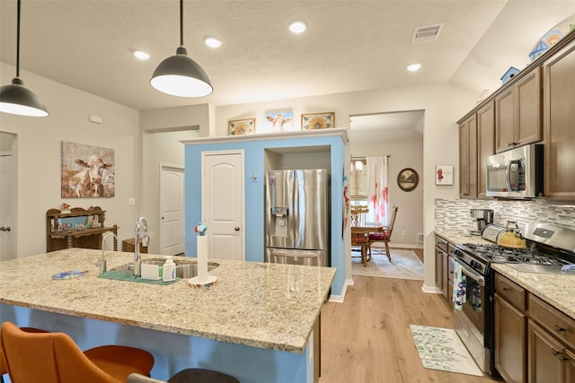 999 Arbor Gln, Conroe, TX 77303 - kitchen with stainless steel appliances, light wood finished floors, a sink, a breakfast bar, and backsplash