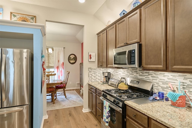 999 Arbor Gln, Conroe, TX 77303 - kitchen featuring appliances with stainless steel finishes, vaulted ceiling, decorative backsplash, light wood-style flooring, and baseboards