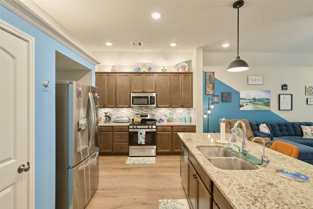 999 Arbor Gln, Conroe, TX 77303 - kitchen featuring appliances with stainless steel finishes, a sink, open floor plan, light wood-style flooring, and backsplash