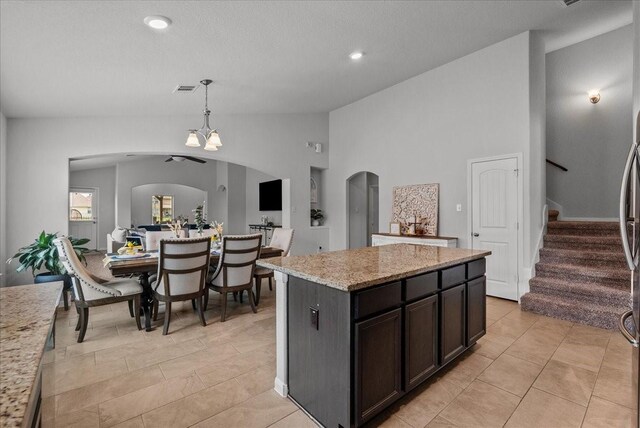 726 Rim Water Dr, Alvin, TX 77511 - kitchen featuring arched walkways, hanging light fixtures, light stone counters, lofted ceiling, and a center island