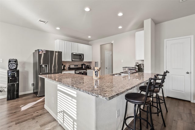 4831 Blue Jacaranda Way, Spring, TX 77373 - kitchen with appliances with stainless steel finishes, a peninsula, light stone counters, light wood-type flooring, and a kitchen bar
