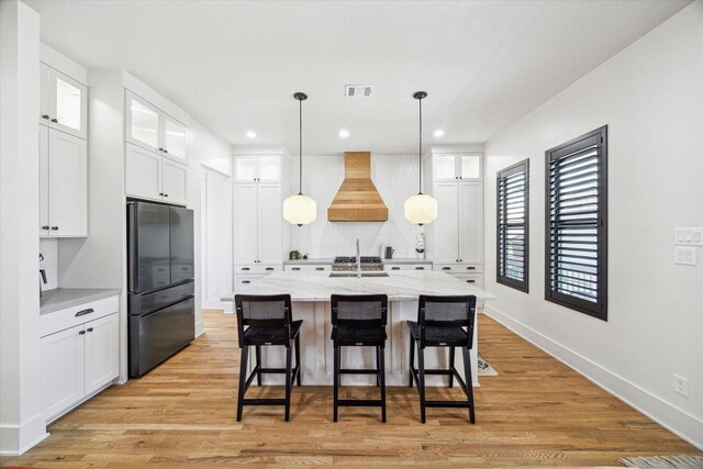 4731 Park Dr, Houston, TX 77023 - kitchen with freestanding refrigerator, custom exhaust hood, a breakfast bar area, white cabinets, and recessed lighting