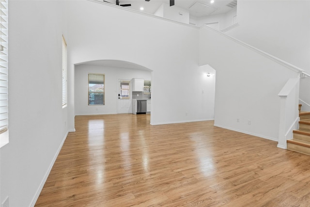 20419 Thunder Ridge Ln, Katy, TX 77449 - unfurnished living room featuring arched walkways, light wood-style flooring, a high ceiling, and stairs