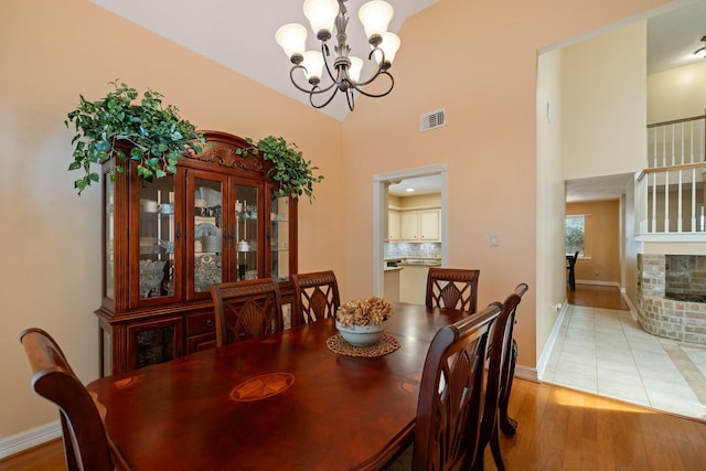 12910 Lake Mist Dr, Cypress, TX 77429 - dining area featuring a chandelier, baseboards, light wood-style flooring, a high ceiling, and a brick fireplace