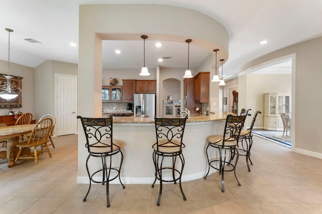25514 Long Iron Ct, Spring, TX 77389 - kitchen with stainless steel fridge, brown cabinets, a breakfast bar area, a peninsula, and light tile patterned floors