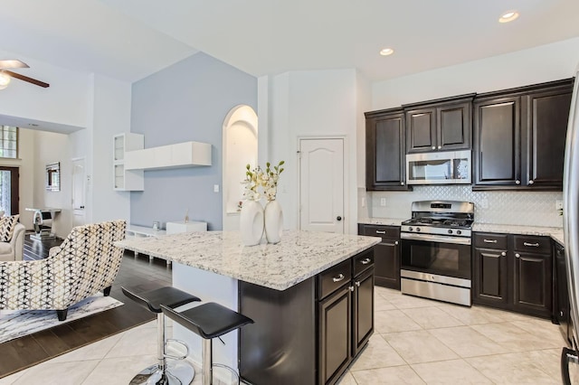 19251 N Cottonwood Green Ln, Cypress, TX 77433 - kitchen featuring stainless steel appliances, ceiling fan, decorative backsplash, a breakfast bar area, and light stone counters