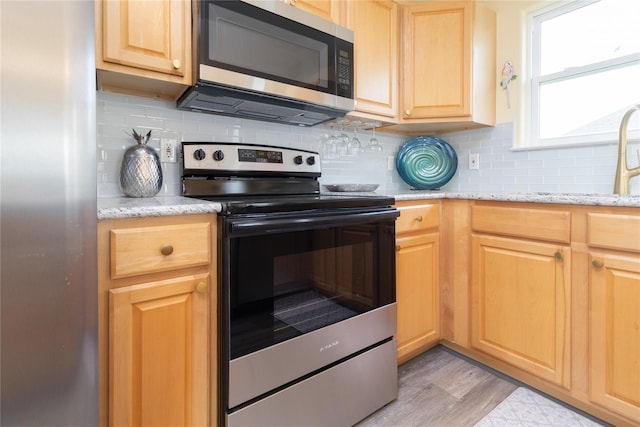4023 Grayson Dr, Galveston, TX 77554 - kitchen featuring stainless steel appliances, tasteful backsplash, light brown cabinetry, light wood-type flooring, and light stone counters