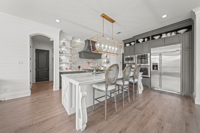 23323 Two Harbors Glen St, Katy, TX 77494 - kitchen featuring built in appliances, open shelves, gray cabinets, a breakfast bar area, and custom range hood