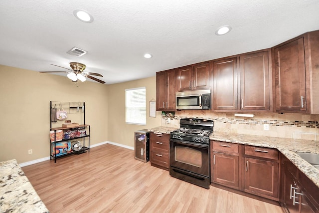 5423 Lillian St, Baytown, TX 77521 - kitchen featuring stainless steel microwave, black gas range oven, decorative backsplash, baseboards, and light wood finished floors