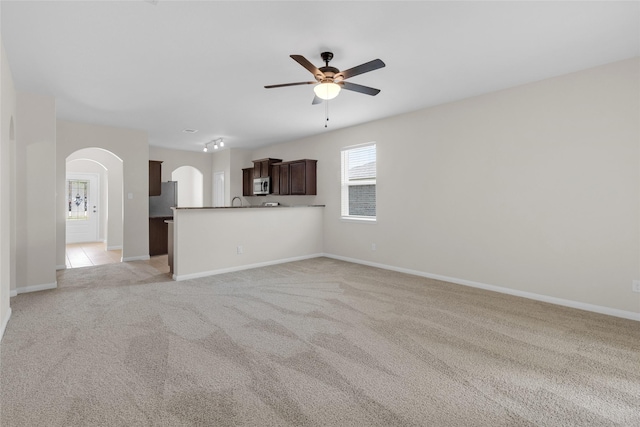 7571 Fettle Ln, Conroe, TX 77304 - unfurnished living room featuring arched walkways, a ceiling fan, light carpet, and baseboards