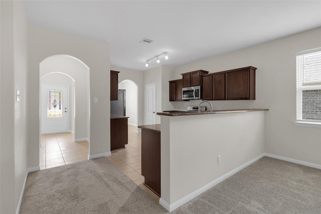 7571 Fettle Ln, Conroe, TX 77304 - kitchen with appliances with stainless steel finishes, arched walkways, light tile patterned floors, light colored carpet, and dark brown cabinets