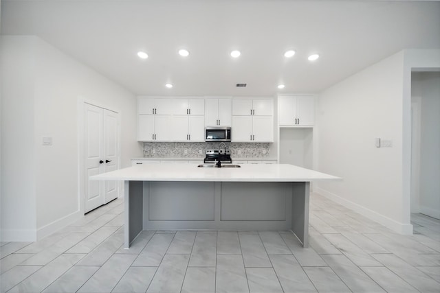 708 Azalea St, Prairie View, TX 77484 - kitchen featuring stainless steel microwave, a kitchen island with sink, light countertops, decorative backsplash, and white cabinets