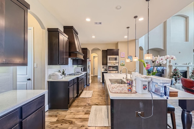 7203 Prairie Grass Ln, Katy, TX 77493 - kitchen featuring arched walkways, a sink, appliances with stainless steel finishes, an island with sink, and light wood-style flooring