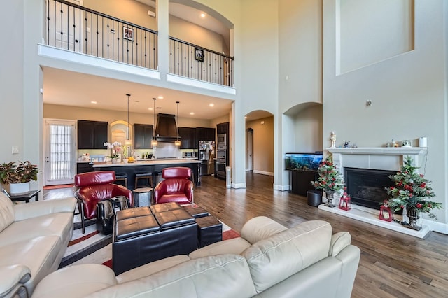 7203 Prairie Grass Ln, Katy, TX 77493 - living area with dark wood-style flooring, a towering ceiling, a fireplace with raised hearth, arched walkways, and baseboards