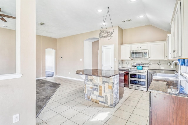7523 Chathan Glen Ln, Richmond, TX 77407 - kitchen featuring stainless steel appliances, arched walkways, a sink, a center island, and dark stone countertops