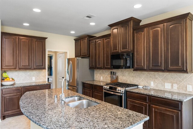 1406 Kallie Hills Ln, Spring, TX 77386 - kitchen featuring appliances with stainless steel finishes, a center island with sink, dark brown cabinets, tasteful backsplash, and a sink
