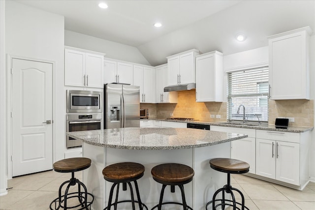 19726 Terrace Cliff Ct, Richmond, TX 77407 - kitchen featuring appliances with stainless steel finishes, a sink, under cabinet range hood, light tile patterned floors, and vaulted ceiling