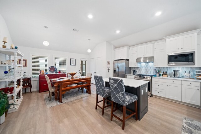 4236 Waterlily Spring Way, Porter, TX 77365 - kitchen featuring appliances with stainless steel finishes, under cabinet range hood, vaulted ceiling, tasteful backsplash, and a center island