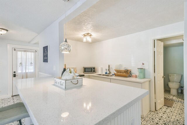 1513 19th St, Galveston, TX 77550 - kitchen featuring a sink, stainless steel microwave, a textured ceiling, white cabinets, and hanging light fixtures