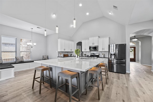 10506 Star Thistle Ct, Cypress, TX 77433 - kitchen featuring stainless steel appliances, arched walkways, backsplash, white cabinets, and a kitchen breakfast bar