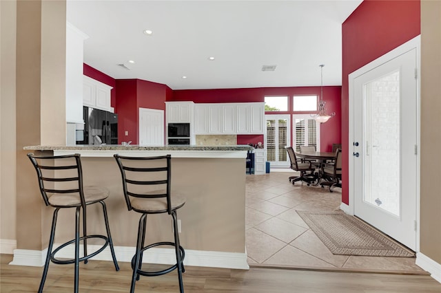 2005 Mistwood Ct, Pearland, TX 77584 - kitchen with black appliances, a peninsula, a breakfast bar, white cabinets, and tasteful backsplash