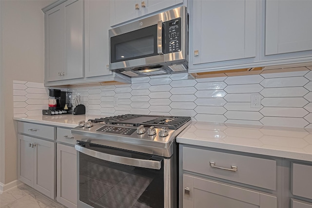 24227 Tallgrass Meadow Trl, Katy, TX 77493 - kitchen featuring appliances with stainless steel finishes, gray cabinetry, light stone countertops, decorative backsplash, and light marble finish flooring