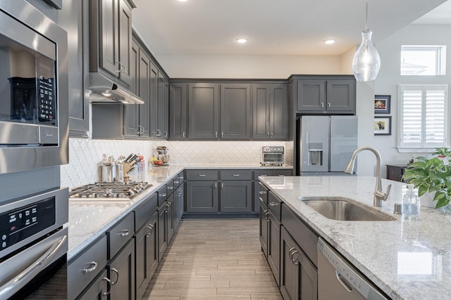 30411 Indigo Falls Dr, Brookshire, TX 77423 - kitchen with stainless steel appliances, a sink, backsplash, hanging light fixtures, and light wood-style flooring