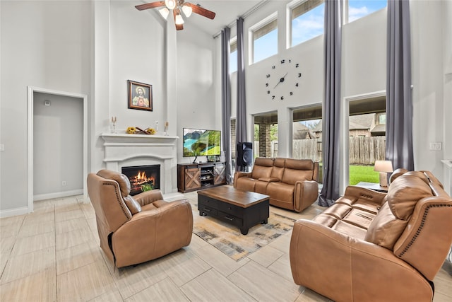 6 Volerran Path Ln, Missouri City, TX 77459 - living area featuring a towering ceiling, a ceiling fan, a warm lit fireplace, and baseboards
