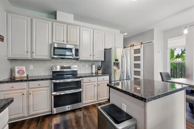 9103 Huckinston Ct, Spring, TX 77379 - kitchen featuring stainless steel appliances, dark wood-style flooring, backsplash, dark stone counters, and a barn door