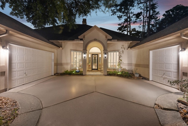 13614 Champions Centre Dr, Houston, TX 77069 - exterior entry at dusk featuring driveway, a garage, stucco siding, and a chimney