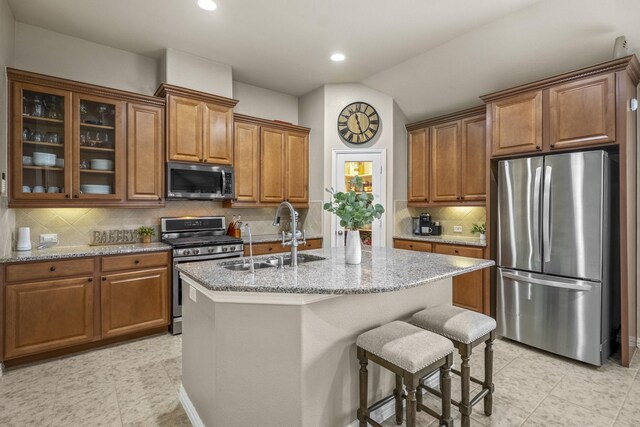 9210 Monarch Field Ln, Cypress, TX 77433 - kitchen featuring stainless steel appliances, brown cabinets, light stone counters, a center island with sink, and recessed lighting