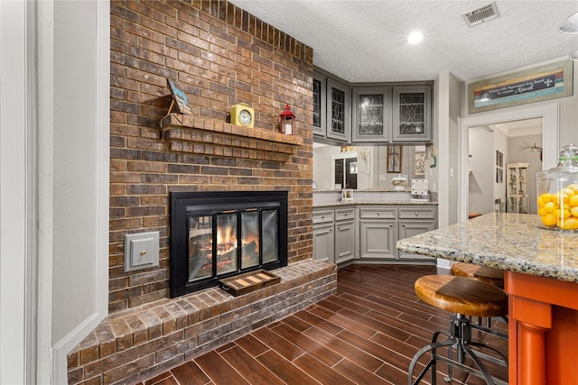 2205 Erin Glen Ct, Deer Park, TX 77536 - kitchen with gray cabinets, glass insert cabinets, a textured ceiling, a fireplace, and light stone countertops