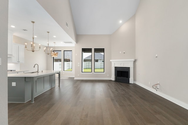 5115 Prairie Gourd Mdw, Manvel, TX 77578 - unfurnished living room featuring a chandelier, a sink, dark wood finished floors, a towering ceiling, and a fireplace with flush hearth