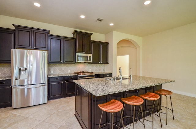 13806 Crystal Harbor Ln, Pearland, TX 77584 - kitchen featuring appliances with stainless steel finishes, a sink, arched walkways, light stone counters, and a breakfast bar