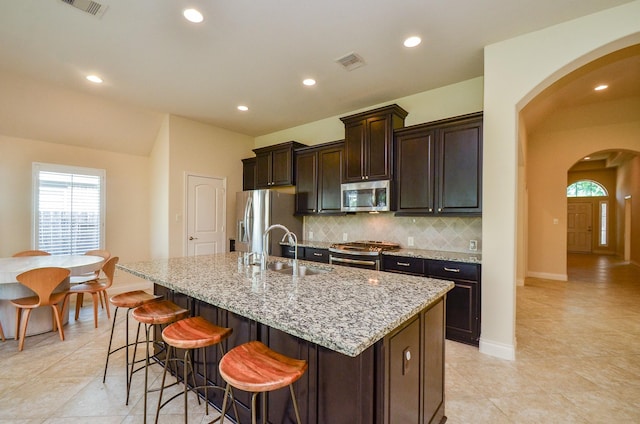 13806 Crystal Harbor Ln, Pearland, TX 77584 - kitchen with appliances with stainless steel finishes, a sink, arched walkways, a kitchen island with sink, and decorative backsplash