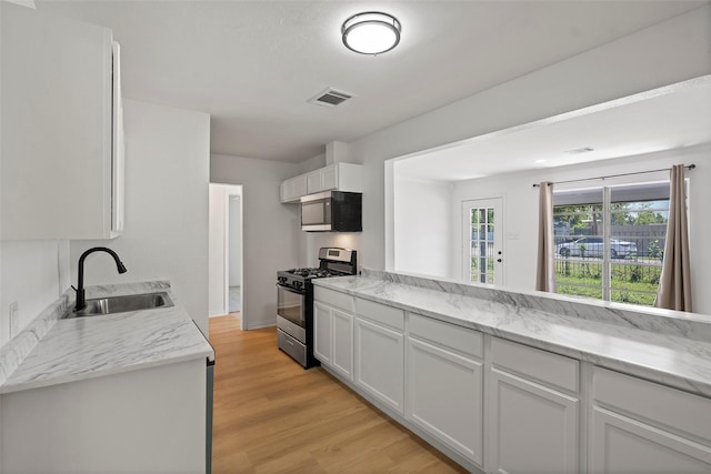 7817 Woodlyn Rd, Houston, TX 77028 - kitchen with stainless steel gas stove, a sink, white cabinetry, light wood-style flooring, and light stone counters