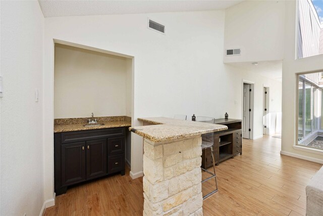 14214 Briarhills Pkwy, Houston, TX 77077 - kitchen with light wood-type flooring, a breakfast bar area, dark cabinets, light stone counters, and high vaulted ceiling