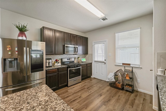23659 Goodfellow Dr, Spring, TX 77373 - kitchen featuring appliances with stainless steel finishes, light wood finished floors, dark brown cabinetry, tasteful backsplash, and light stone counters