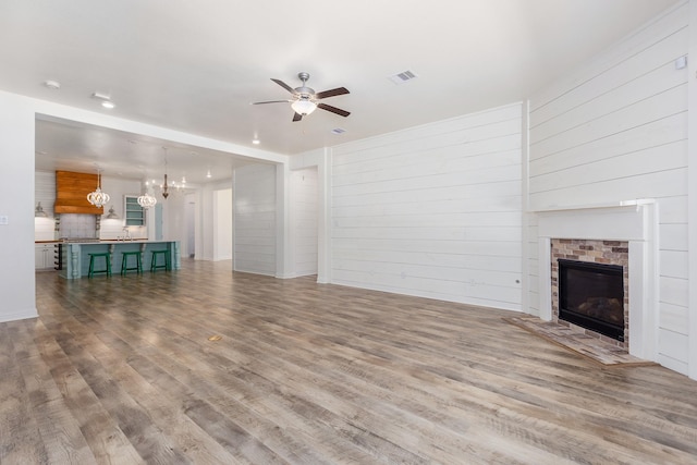 19276 Yellow Chestnut Ln, New Caney, TX 77357 - unfurnished living room with a chandelier, ceiling fan, wood finished floors, a brick fireplace, and wood walls